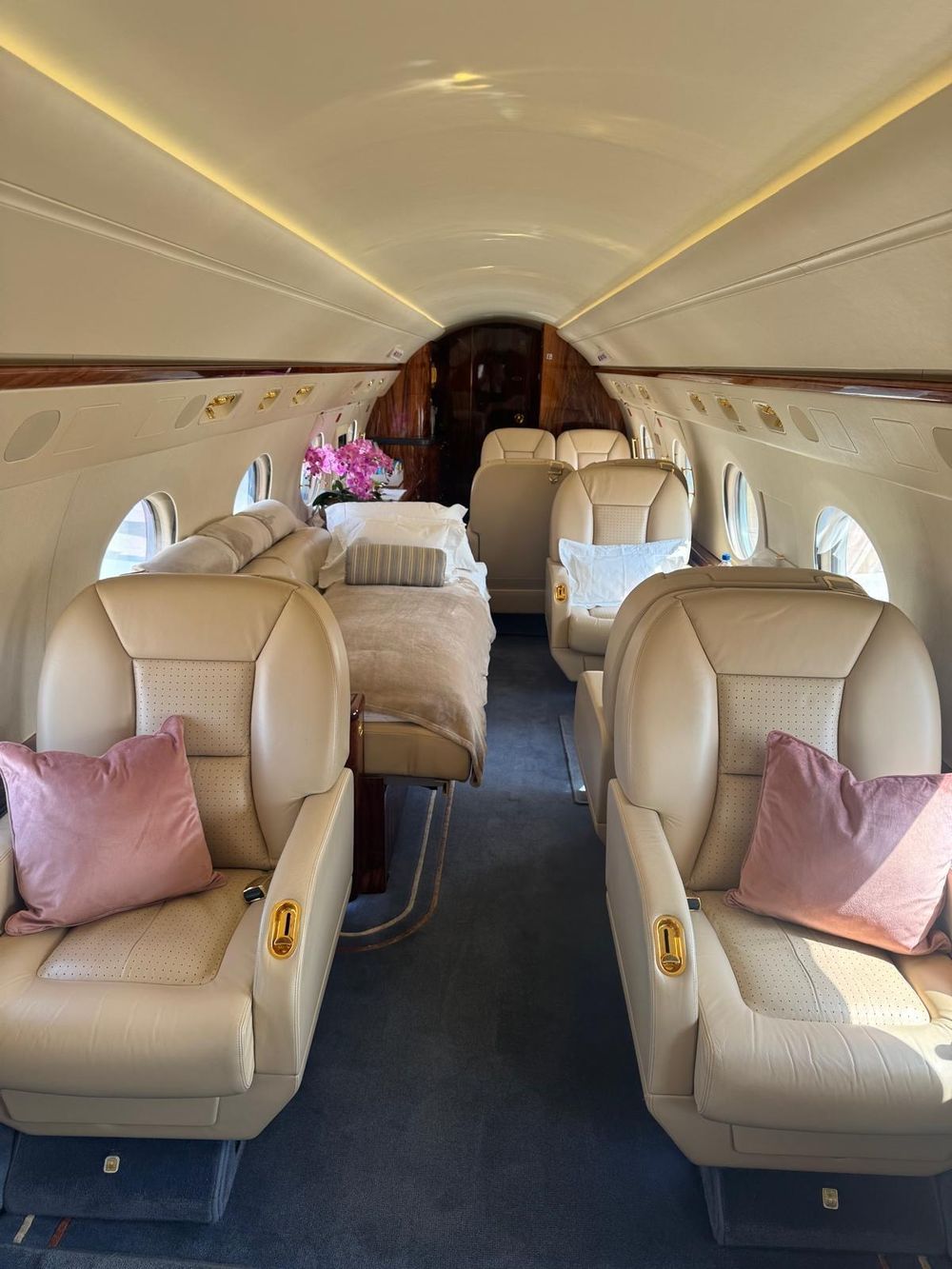Business-jet cabin with cream leather seats, a bed made up with white linen and orchids by the window