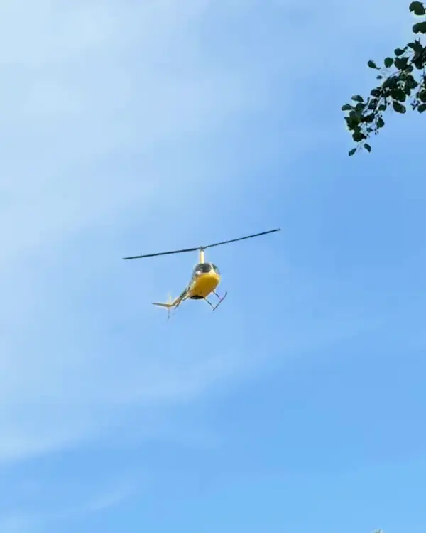 A yellow helicopter in flight against a summer sky