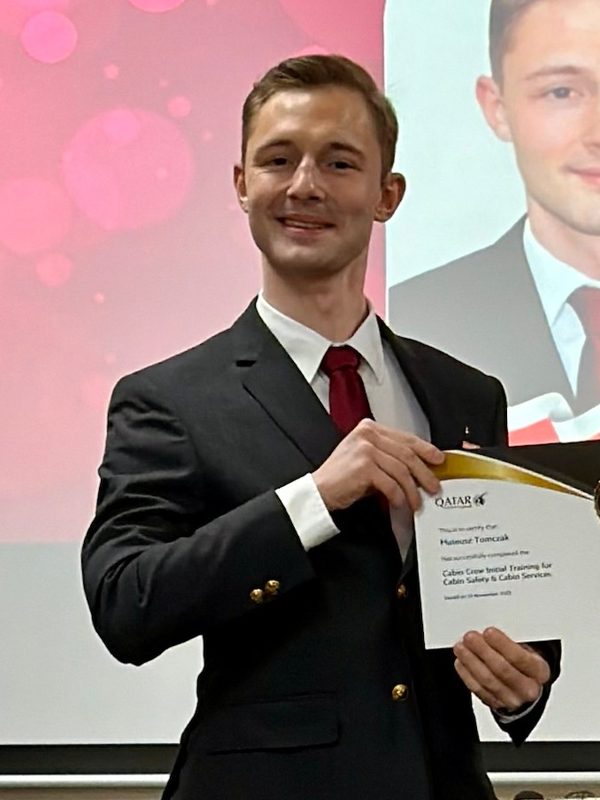 Mateusz Tomczak in a dark suit holding his Qatar Airways training certificate